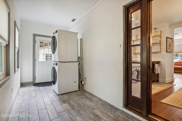 laundry room featuring crown molding, stacked washer / dryer, and light hardwood / wood-style flooring