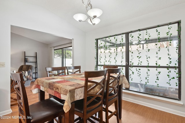 dining space with wood-type flooring, an inviting chandelier, and lofted ceiling