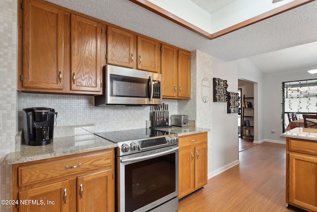 kitchen featuring light stone countertops, a textured ceiling, stainless steel appliances, light hardwood / wood-style flooring, and lofted ceiling