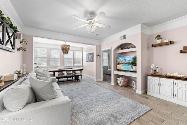 living room featuring ceiling fan with notable chandelier, ornamental molding, a textured ceiling, built in features, and light hardwood / wood-style floors