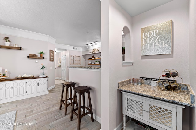 bar with a textured ceiling, stone counters, and light hardwood / wood-style flooring