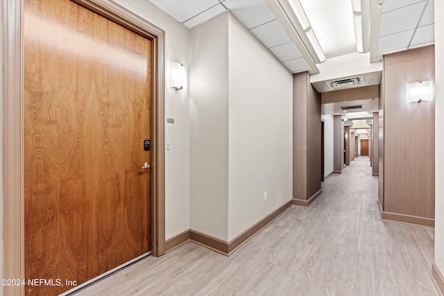 corridor with a drop ceiling and light wood-type flooring