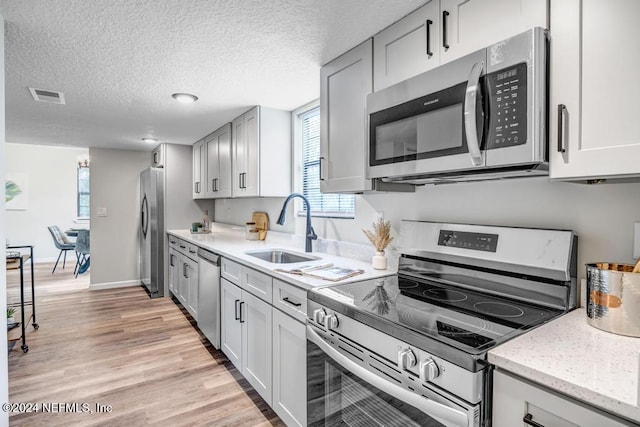 kitchen with light hardwood / wood-style flooring, sink, appliances with stainless steel finishes, and a textured ceiling