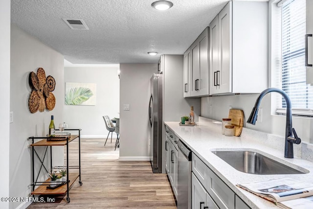 kitchen with appliances with stainless steel finishes, a textured ceiling, light hardwood / wood-style flooring, and sink