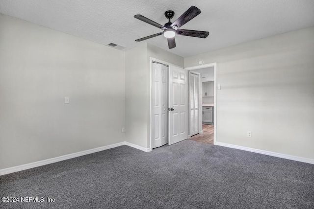 unfurnished bedroom with ceiling fan, dark carpet, and a textured ceiling