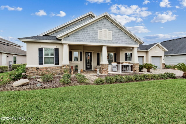 craftsman-style home with stucco siding, covered porch, an attached garage, a front yard, and stone siding