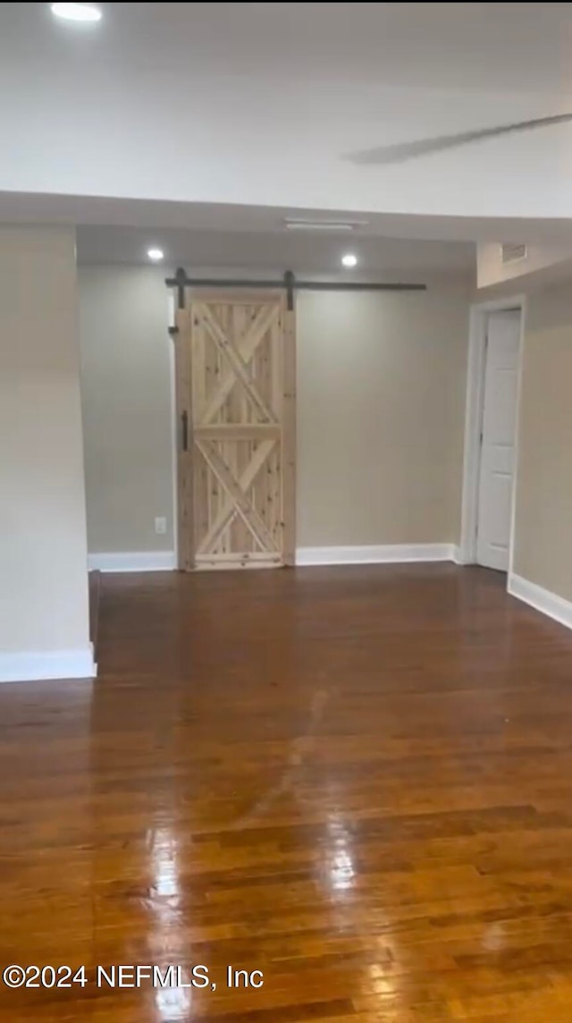 unfurnished room with a barn door and dark wood-type flooring