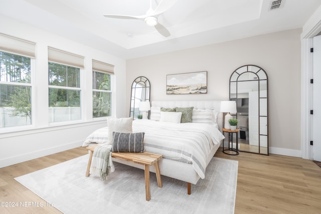 bedroom with a raised ceiling, light hardwood / wood-style flooring, and ceiling fan