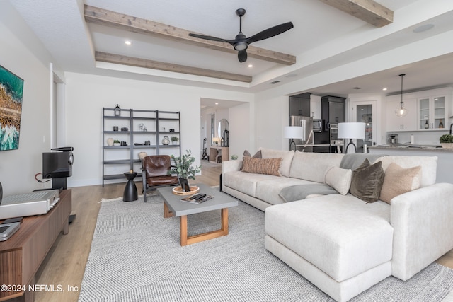 living room featuring beamed ceiling, ceiling fan, a raised ceiling, and light wood-type flooring