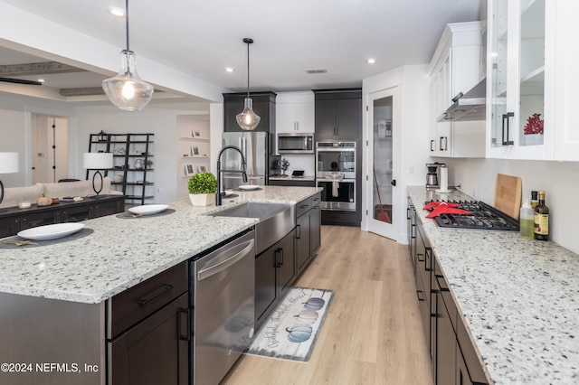 kitchen with white cabinets, hanging light fixtures, an island with sink, appliances with stainless steel finishes, and light hardwood / wood-style floors