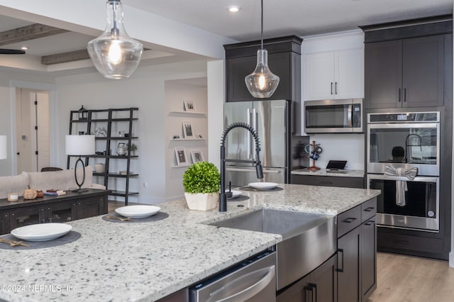 kitchen with light stone countertops, stainless steel appliances, decorative light fixtures, and light hardwood / wood-style floors