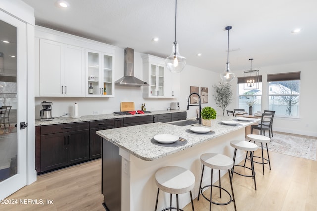 kitchen featuring sink, wall chimney range hood, a center island with sink, white cabinets, and light hardwood / wood-style floors