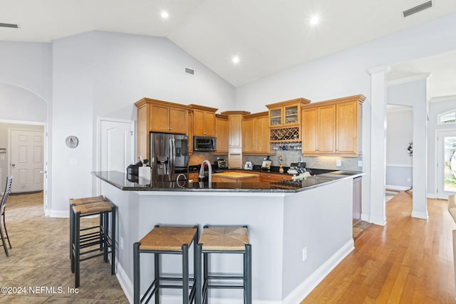 kitchen with decorative backsplash, appliances with stainless steel finishes, light hardwood / wood-style flooring, dark stone countertops, and a breakfast bar area