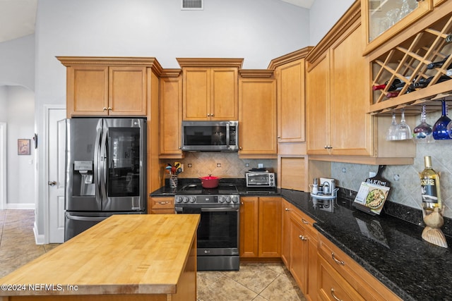 kitchen featuring wood counters, tasteful backsplash, high vaulted ceiling, light tile patterned floors, and appliances with stainless steel finishes