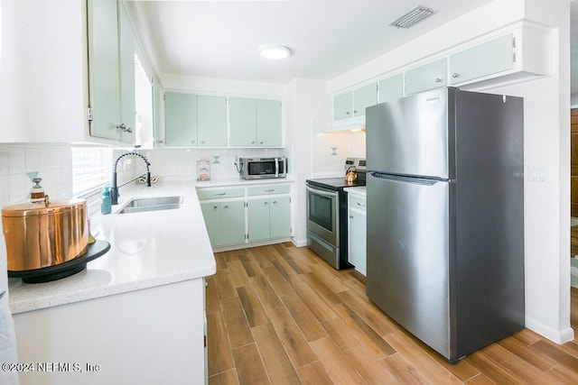 kitchen with sink, backsplash, appliances with stainless steel finishes, and light hardwood / wood-style flooring