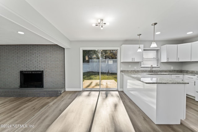 kitchen with light stone counters, white cabinets, decorative light fixtures, and a brick fireplace