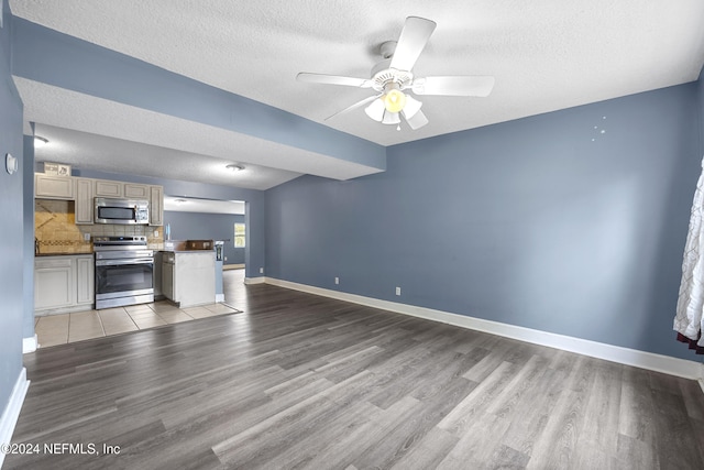 unfurnished living room with a textured ceiling, light wood-type flooring, and ceiling fan