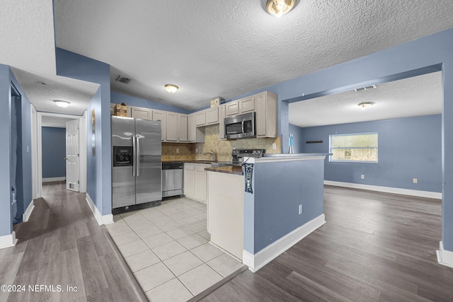 kitchen featuring sink, light hardwood / wood-style flooring, a textured ceiling, kitchen peninsula, and stainless steel appliances