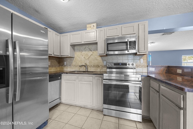 kitchen with a textured ceiling, stainless steel appliances, sink, light tile patterned floors, and white cabinetry