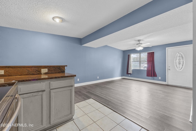 kitchen featuring ceiling fan, stainless steel range with electric stovetop, a textured ceiling, gray cabinets, and light wood-type flooring