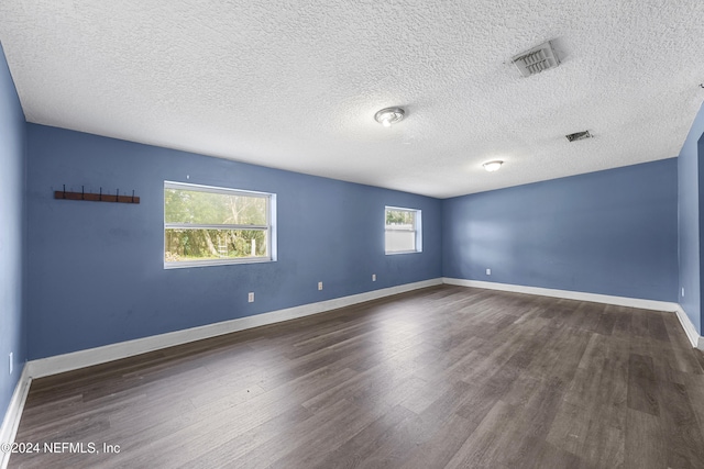 empty room featuring a textured ceiling, dark hardwood / wood-style flooring, and plenty of natural light