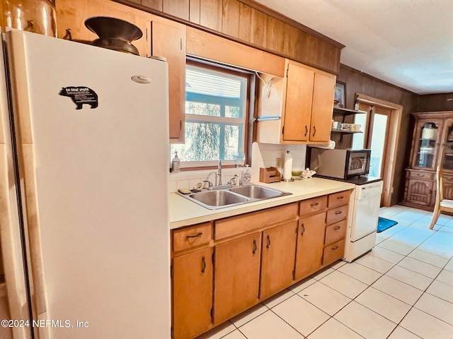 kitchen with wood walls, sink, white fridge, and light tile patterned floors