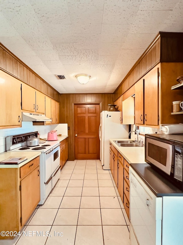 kitchen featuring light tile patterned flooring, white appliances, wood walls, and sink