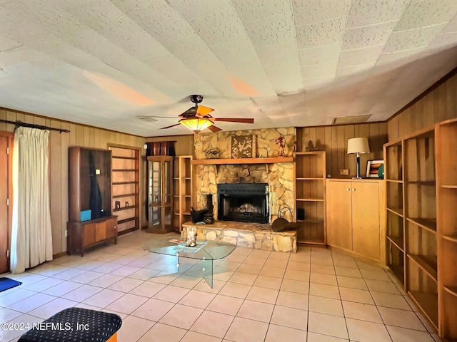 unfurnished living room with a stone fireplace, wood walls, ceiling fan, and light tile patterned floors