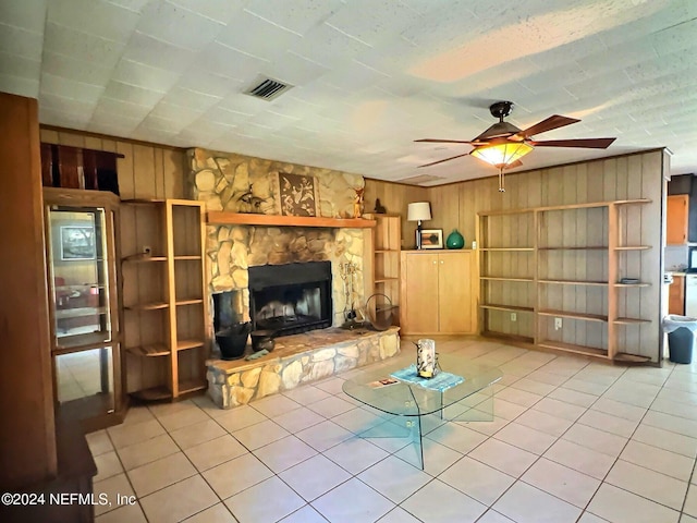 unfurnished living room featuring ceiling fan, light tile patterned flooring, a fireplace, and wooden walls