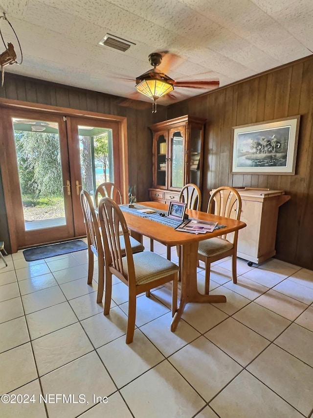 tiled dining room featuring french doors, ceiling fan, and wood walls