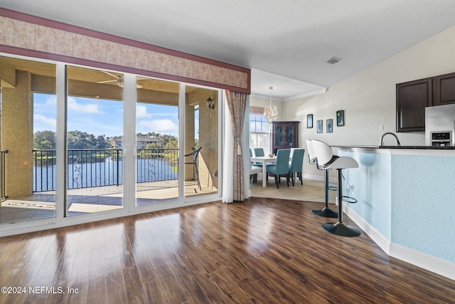 interior space with dark brown cabinetry, an inviting chandelier, stainless steel fridge, a water view, and hardwood / wood-style flooring