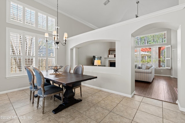 tiled dining room featuring a healthy amount of sunlight, ornamental molding, high vaulted ceiling, and a chandelier