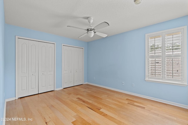 unfurnished bedroom featuring a textured ceiling, ceiling fan, light hardwood / wood-style floors, and two closets