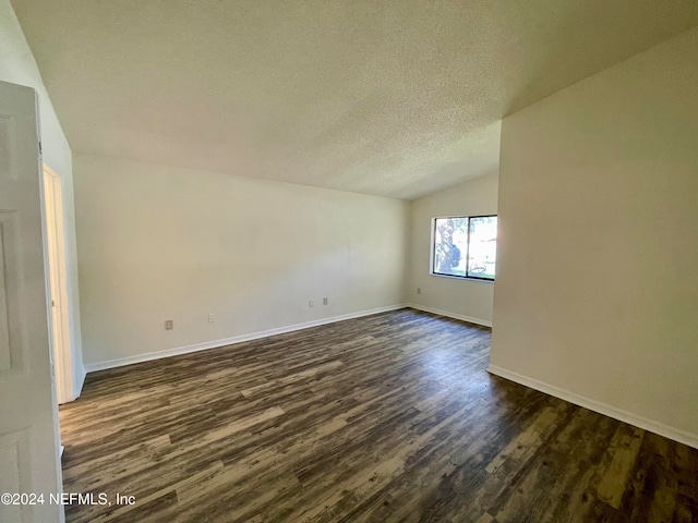 spare room with a textured ceiling, dark wood-type flooring, and vaulted ceiling