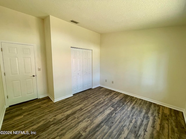 unfurnished bedroom with a textured ceiling, dark wood-type flooring, and a closet