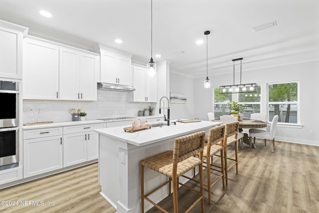 kitchen featuring pendant lighting, stainless steel double oven, a kitchen island with sink, and white cabinets