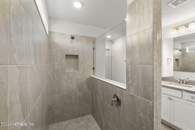 bathroom with a tile shower, vanity, and a textured ceiling