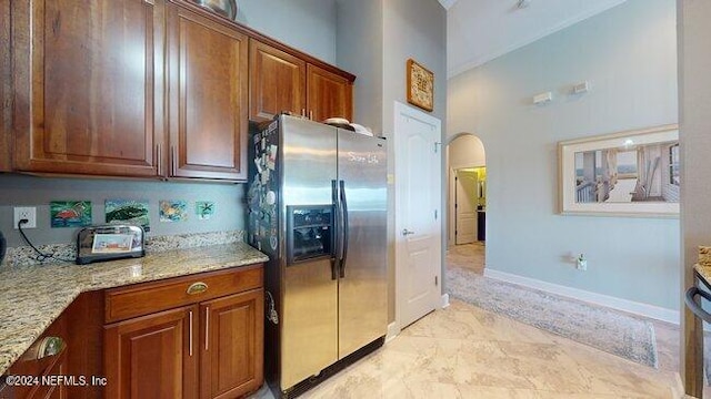 kitchen with light stone countertops, stainless steel fridge with ice dispenser, and a high ceiling