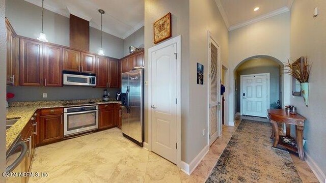 kitchen with appliances with stainless steel finishes, a towering ceiling, pendant lighting, light stone counters, and crown molding