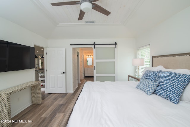 bedroom featuring ceiling fan, a barn door, wood-type flooring, and a tray ceiling