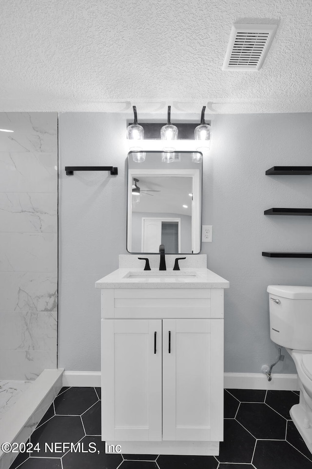 bathroom featuring tile patterned floors, a textured ceiling, vanity, tiled shower, and toilet