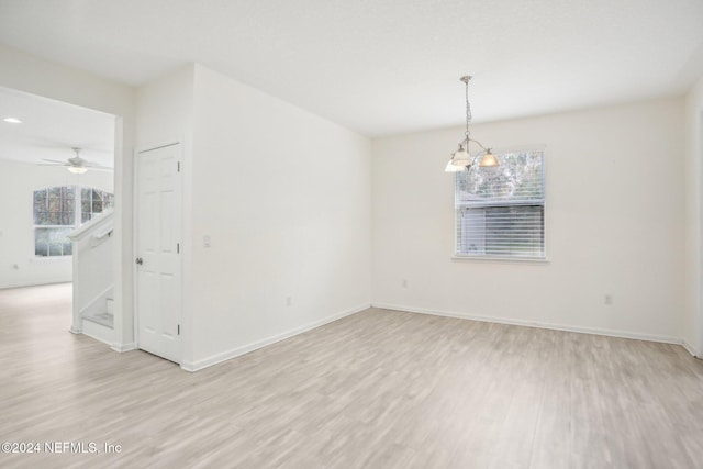 spare room with ceiling fan with notable chandelier and light hardwood / wood-style flooring