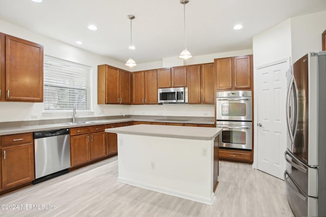 kitchen with appliances with stainless steel finishes, sink, decorative light fixtures, light hardwood / wood-style floors, and a kitchen island