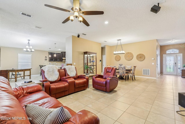 tiled living room with ceiling fan with notable chandelier and a textured ceiling