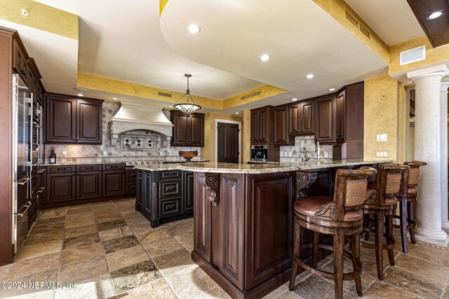 kitchen with pendant lighting, a raised ceiling, dark brown cabinets, and ornate columns