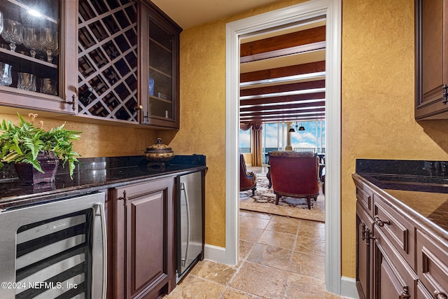 bar featuring dark stone countertops, dark brown cabinetry, and beverage cooler