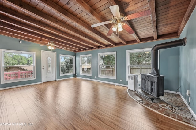 unfurnished living room with a wood stove, lofted ceiling with beams, hardwood / wood-style floors, and a healthy amount of sunlight