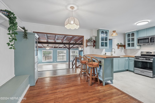 kitchen with blue cabinetry, pendant lighting, stainless steel appliances, and light hardwood / wood-style floors