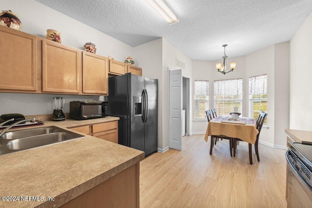 kitchen featuring sink, a notable chandelier, pendant lighting, light hardwood / wood-style floors, and black appliances