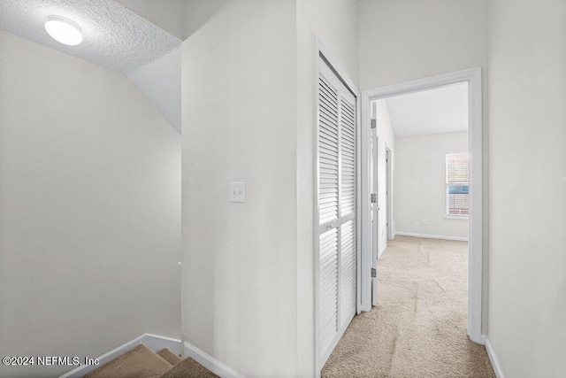 corridor with vaulted ceiling, light carpet, and a textured ceiling